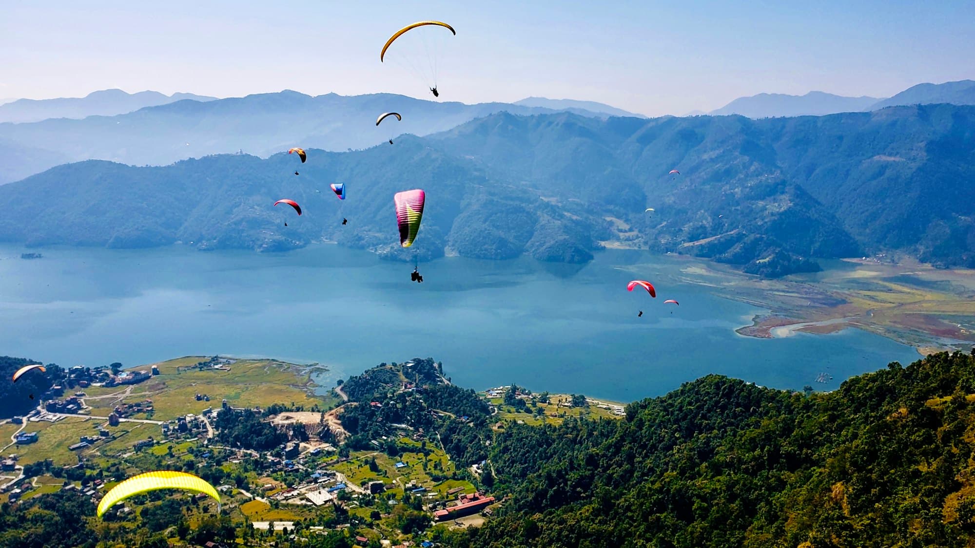 Paragliders above Phewa Lake with hills and the city below