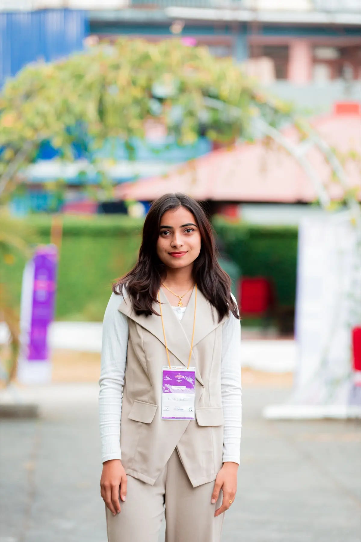 Smiling attendee wearing an event badge standing outdoors on the venue grounds, with a garden arch behind