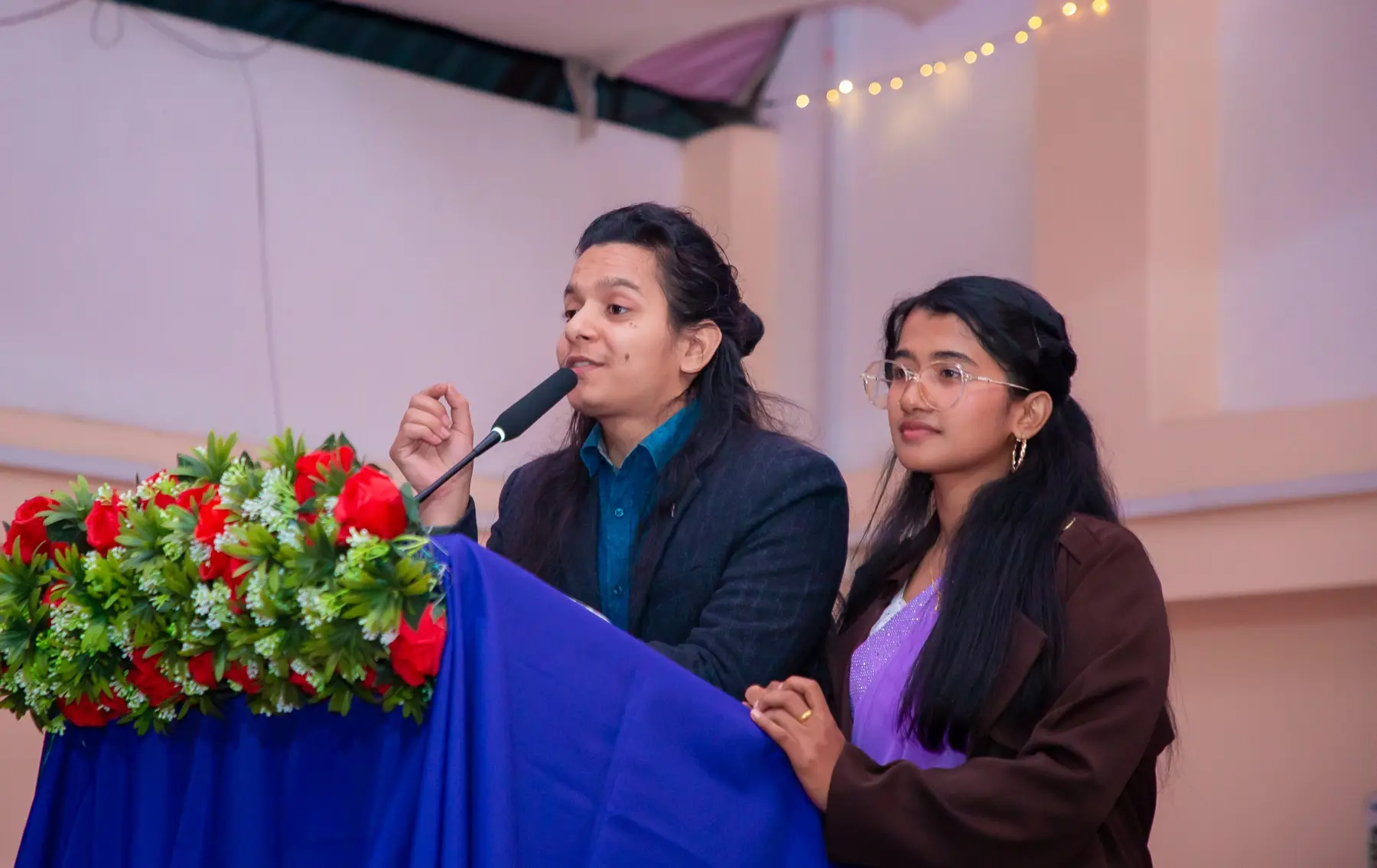 Two hosts speaking at a podium decorated with red and white flowers