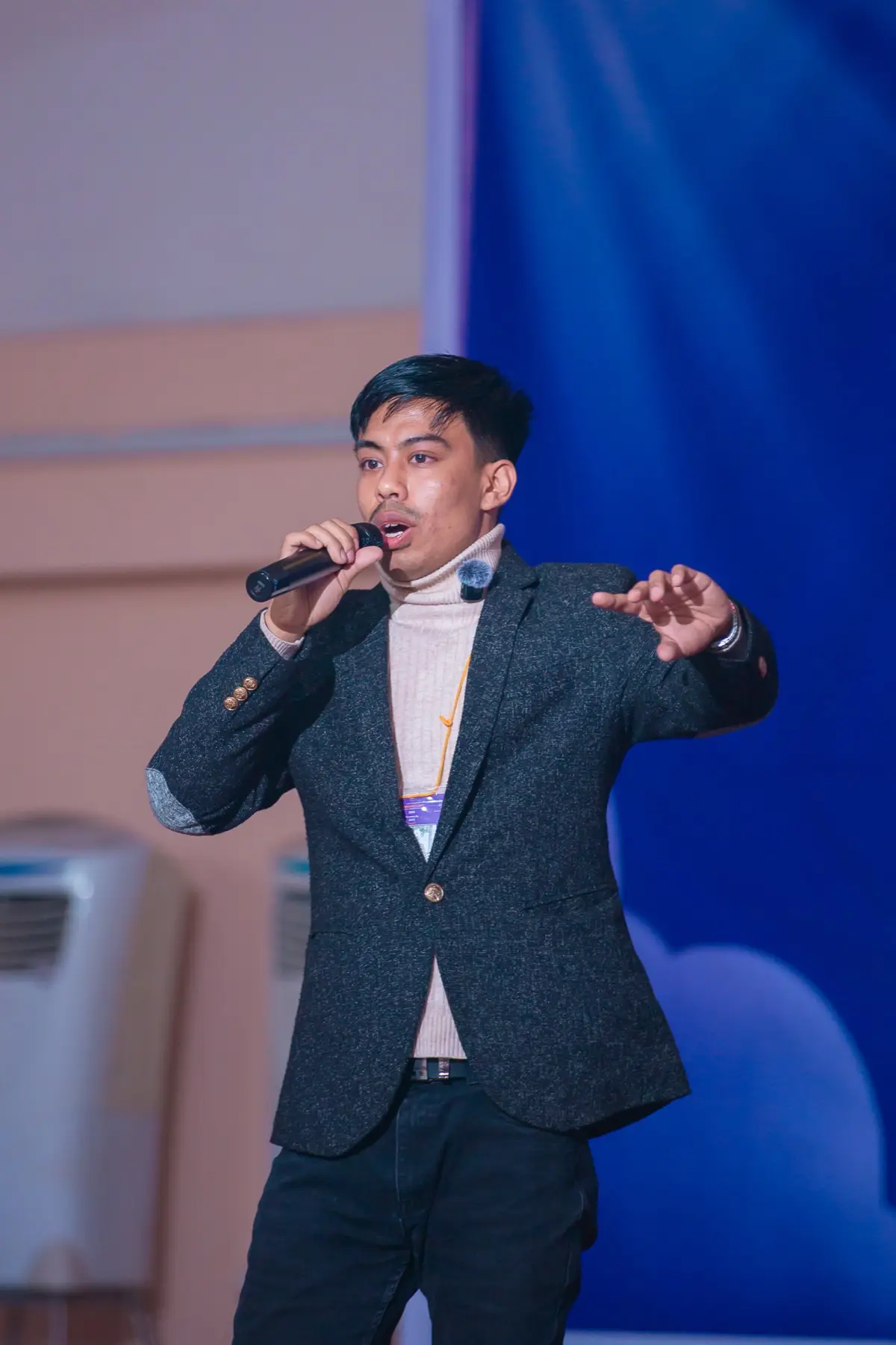 Speaker in a dark blazer gesturing while talking into a microphone on stage