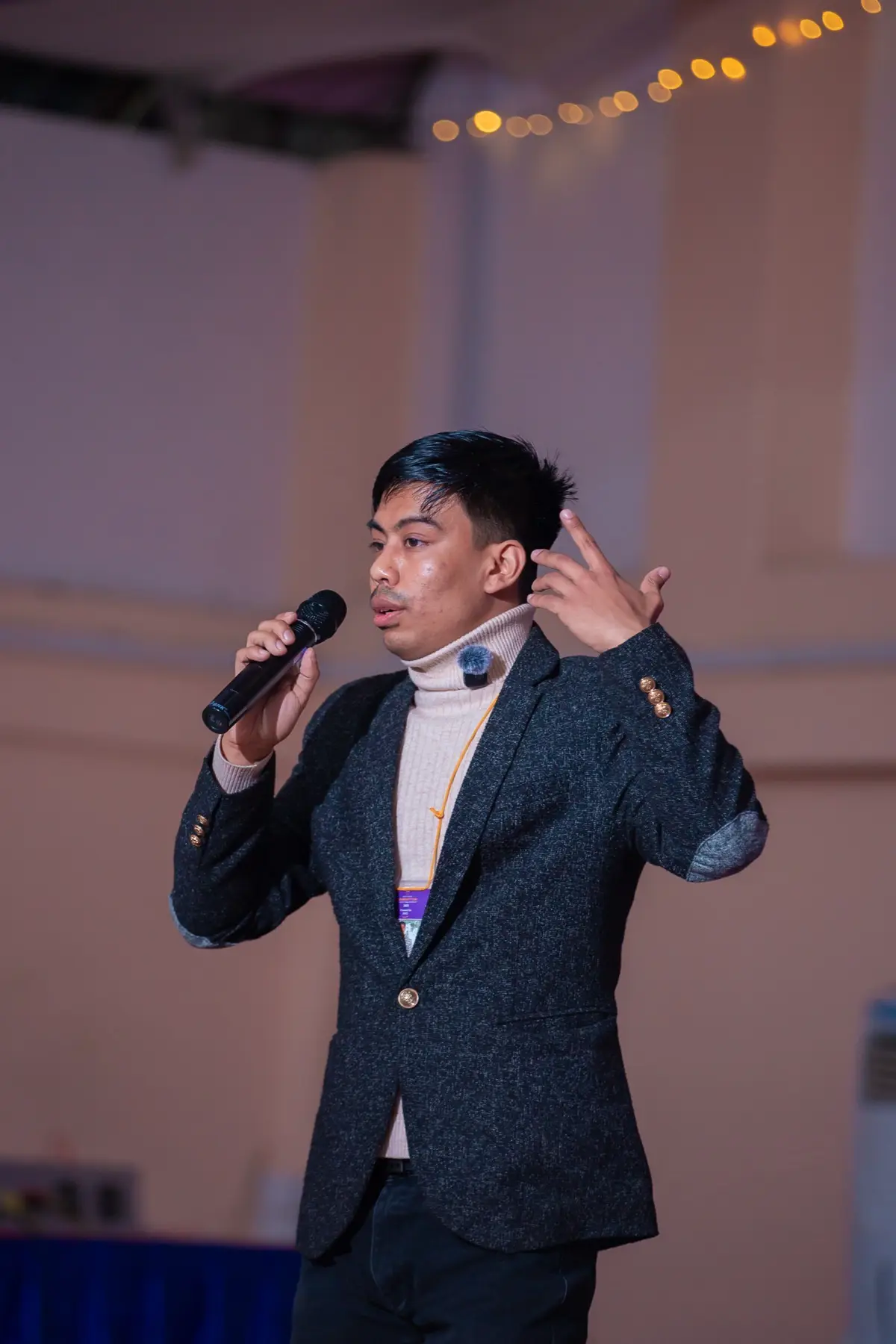 Presenter in a dark blazer holding a microphone and gesturing on stage