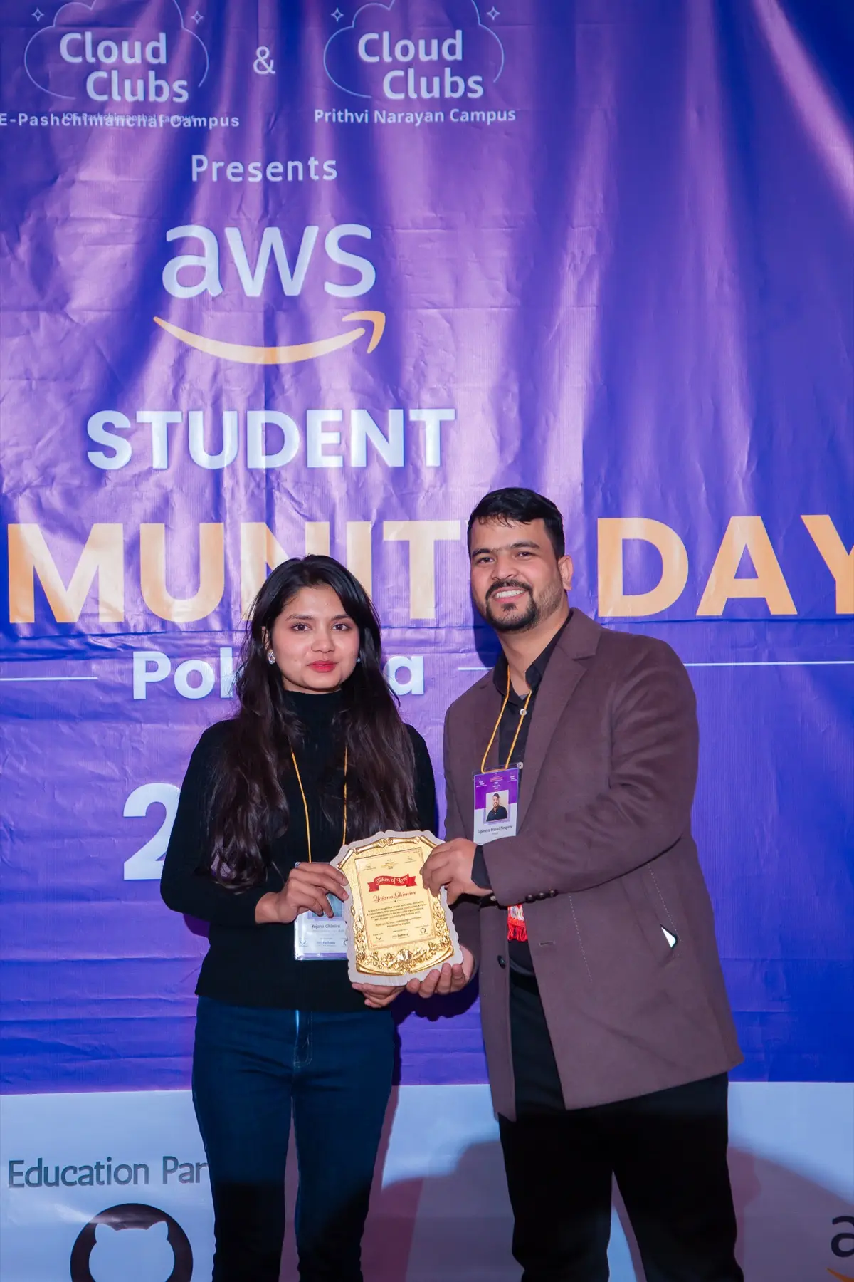 Two people in front of the event backdrop holding a golden plaque between them