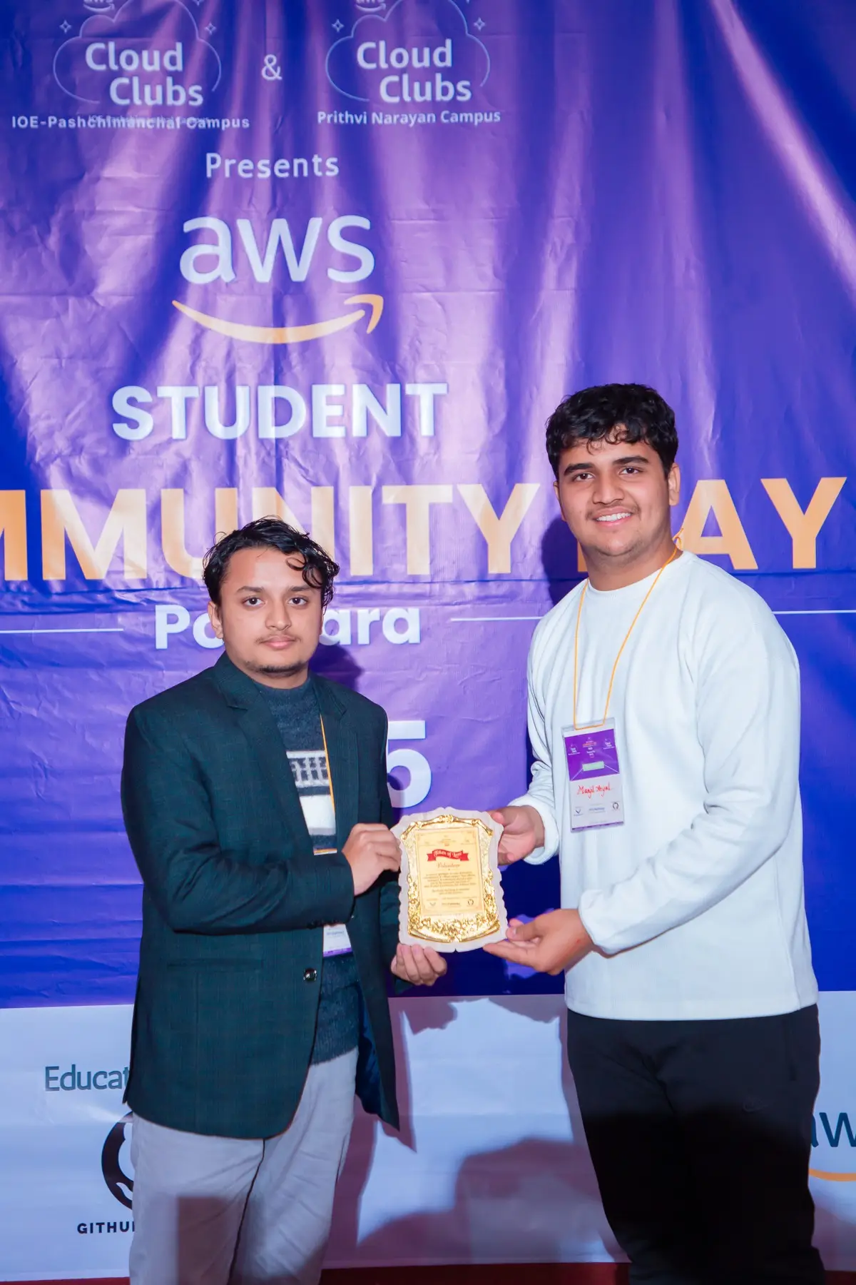 Two people shaking hands over a plaque in front of the event backdrop