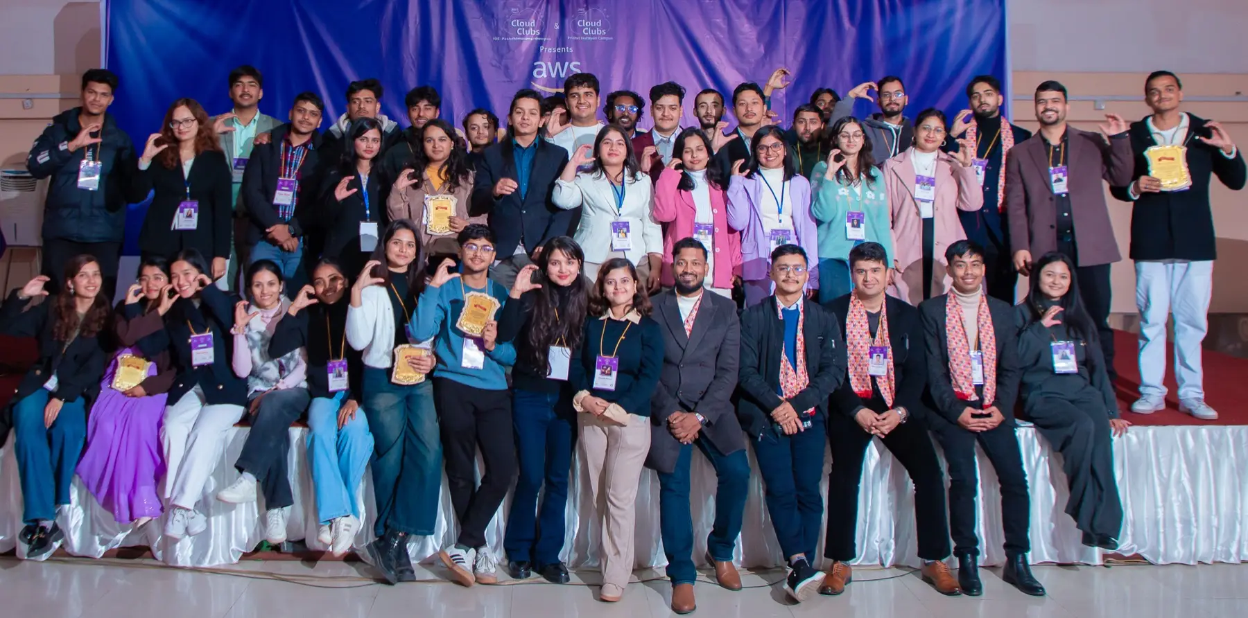 Large group of volunteers and attendees posed together on stage in front of the backdrop, many holding plaques